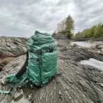 Tenzing backpack in green sitting on rocks at the coast